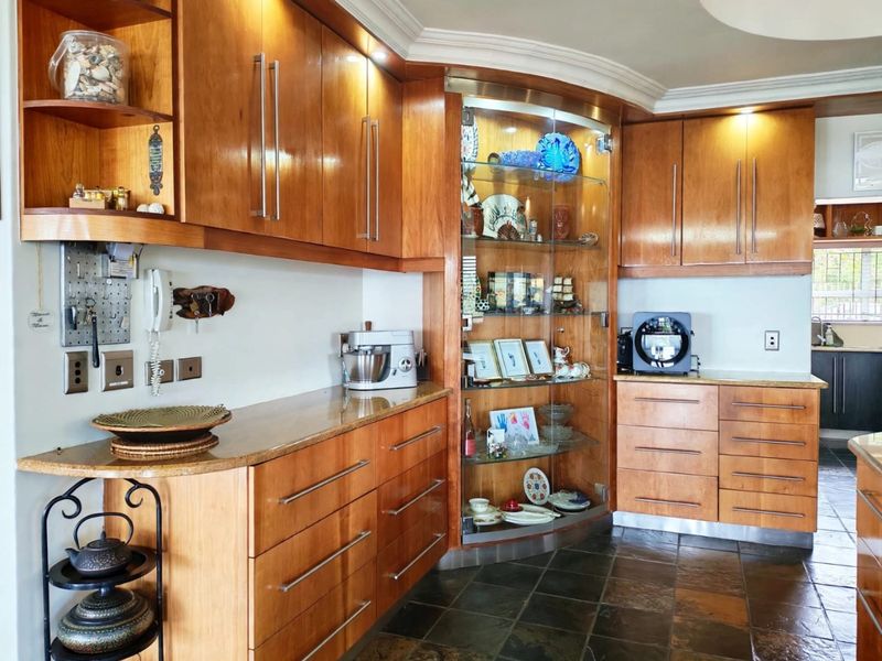 A well-maintained kitchen featuring warm-toned wooden cabinetry, granite countertops, a built-in glass display cabinet, and durable slate flooring.
