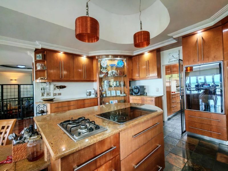 Spacious kitchen featuring warm wooden cabinetry, granite countertops, a central island with dual hobs, and a unique recessed ceiling dome with pendant lighting.