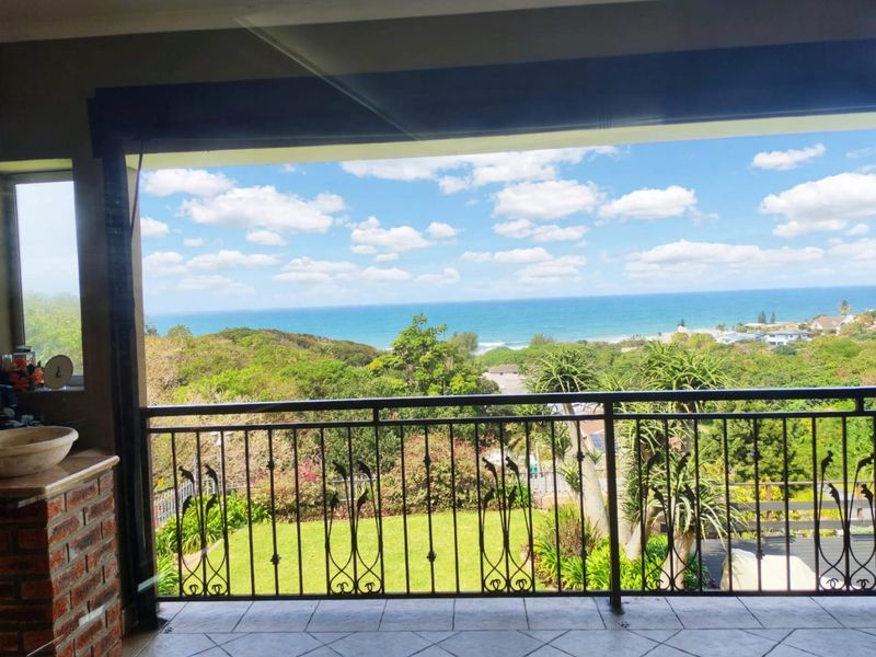 A covered balcony featuring a decorative wrought iron balustrade and tiled flooring, offering expansive elevated views of the surrounding landscape and ocean.