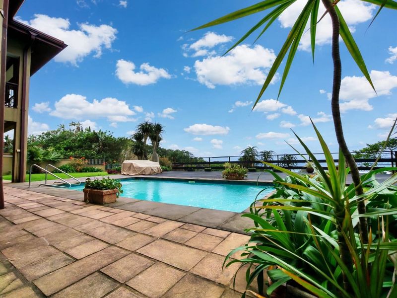 Outdoor pool area featuring a paved patio, wooden decking, and a swimming pool with a metal handrail, set against a landscaped garden backdrop.