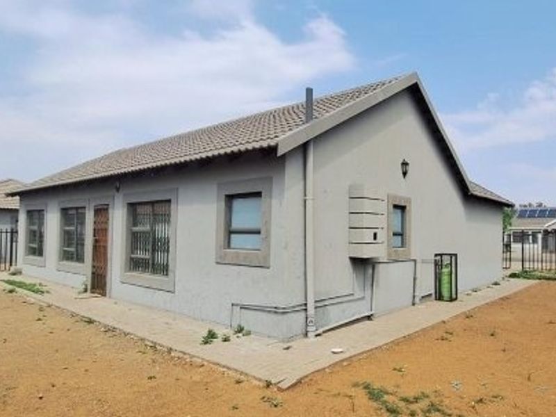 Rear view of a single-story house featuring a tiled roof, security bars on windows, and a paved perimeter walkway.