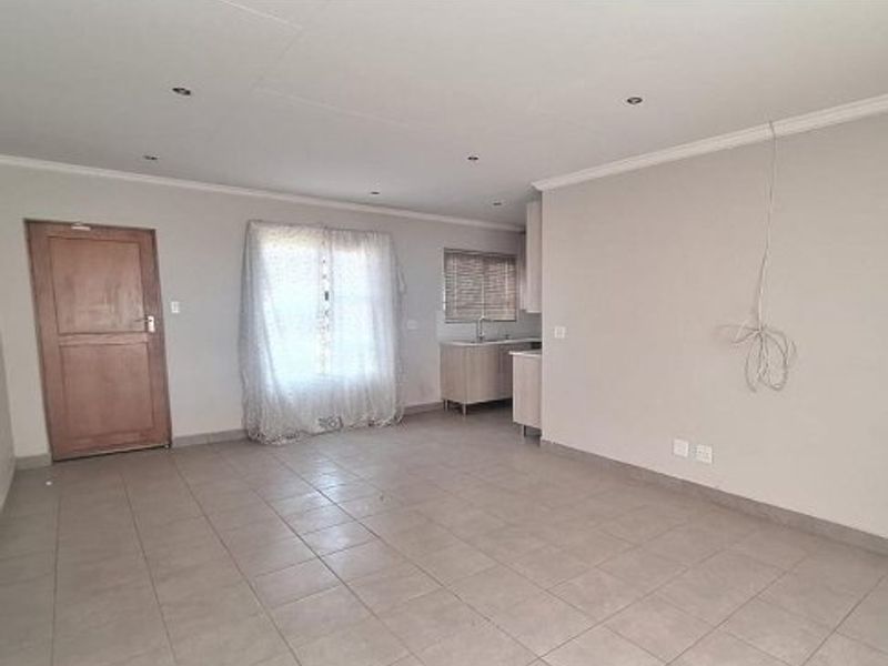 An open-plan living area featuring tiled flooring, recessed lighting, and a compact kitchen corner with built-in cabinetry and sink.