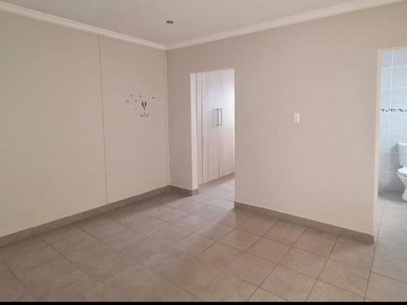 An empty bedroom featuring tiled flooring, built-in cupboards, and an adjoining en-suite bathroom with a toilet.