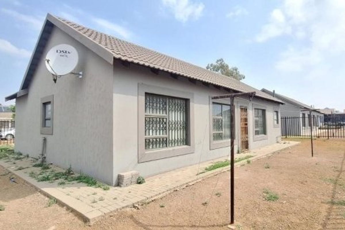 Rear view of a single-story residential house featuring a tiled roof, security bars on windows, and a paved walkway surrounding the structure.
