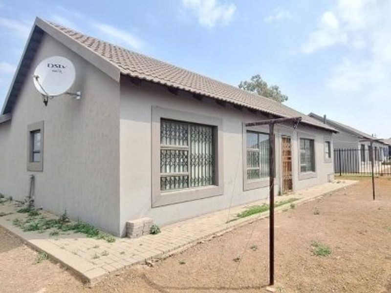 Rear view of a single-story residential house featuring a tiled roof, security bars on windows, and a paved walkway surrounding the structure.