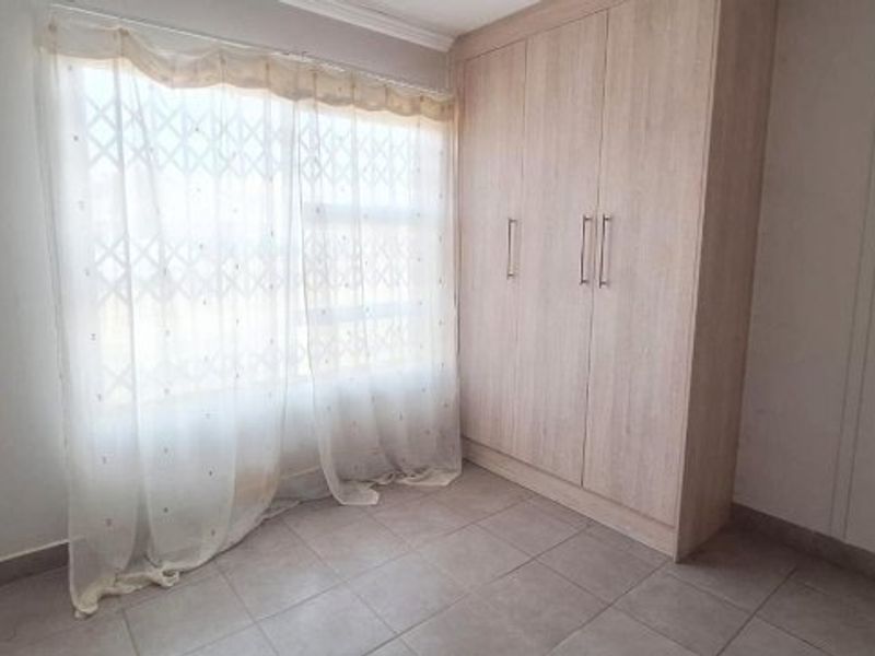 A bright, empty bedroom featuring neutral tiled flooring and a large, light-wood built-in wardrobe with ample storage space.