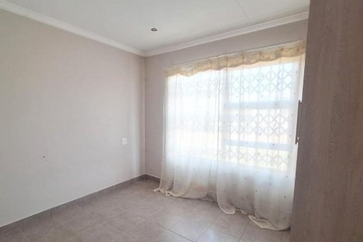 A bright, empty bedroom featuring tiled flooring, recessed ceiling lighting, and a built-in cupboard, offering a clean canvas for personalization.