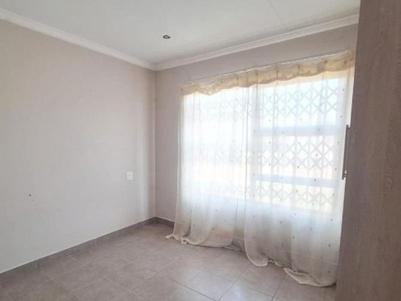 A bright, empty bedroom featuring tiled flooring, recessed ceiling lighting, and a built-in cupboard, offering a clean canvas for personalization.