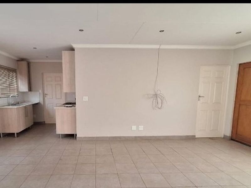 An open-plan living and kitchen area featuring tiled flooring, recessed lighting, and functional kitchen cabinetry with a built-in hob and sink.