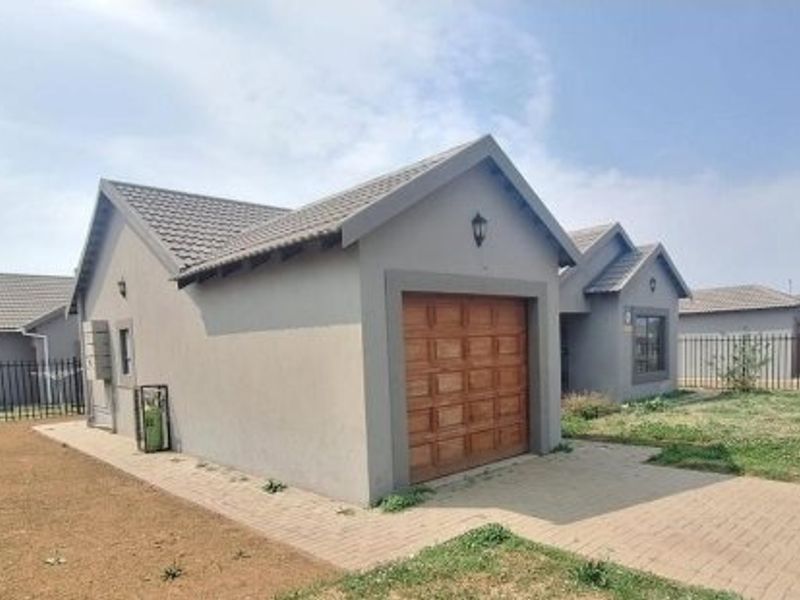 A well-maintained single-story house featuring a tiled roof, a wooden garage door, and a paved driveway, set within a fenced residential property.