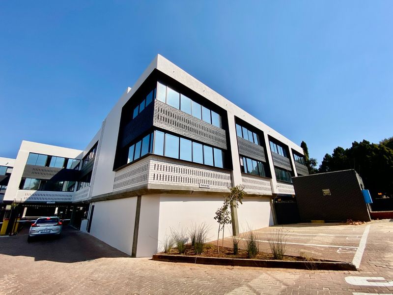 Modern commercial office building featuring a contemporary facade with extensive glazing, brick detailing, and a paved parking area with dedicated delivery access.