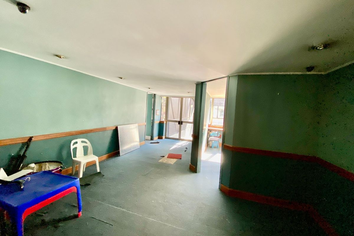 An open-plan commercial space featuring green painted walls with timber dado rails, recessed lighting, and worn carpeting, leading to a glass sliding door entrance.