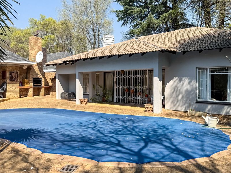 Outdoor pool area featuring a paved patio, built-in brick braai, and a covered terrace, ideal for entertaining.