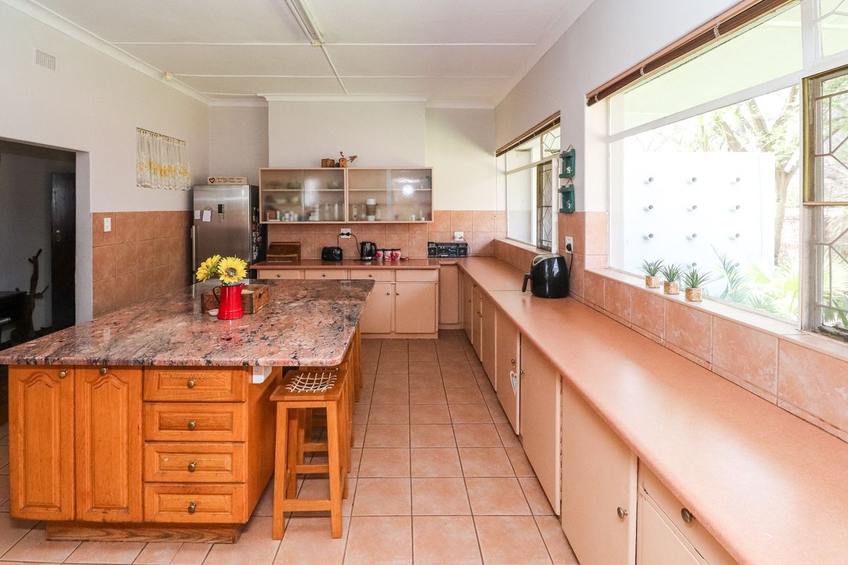 Spacious kitchen featuring a large granite-topped island, extensive built-in cabinetry, tiled flooring, and ample natural light from large windows.