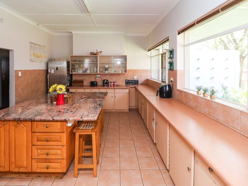 Spacious kitchen featuring a large granite-topped island, extensive built-in cabinetry, tiled flooring, and ample natural light from large windows.