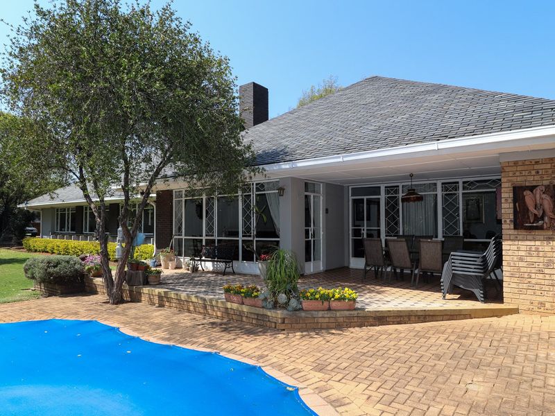 Rear view of the property featuring a covered patio, brick paving, and a swimming pool with a cover.