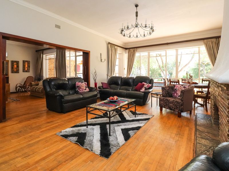 Spacious open-plan living area featuring polished hardwood floors, a prominent brick fireplace, and large windows that provide ample natural light.
