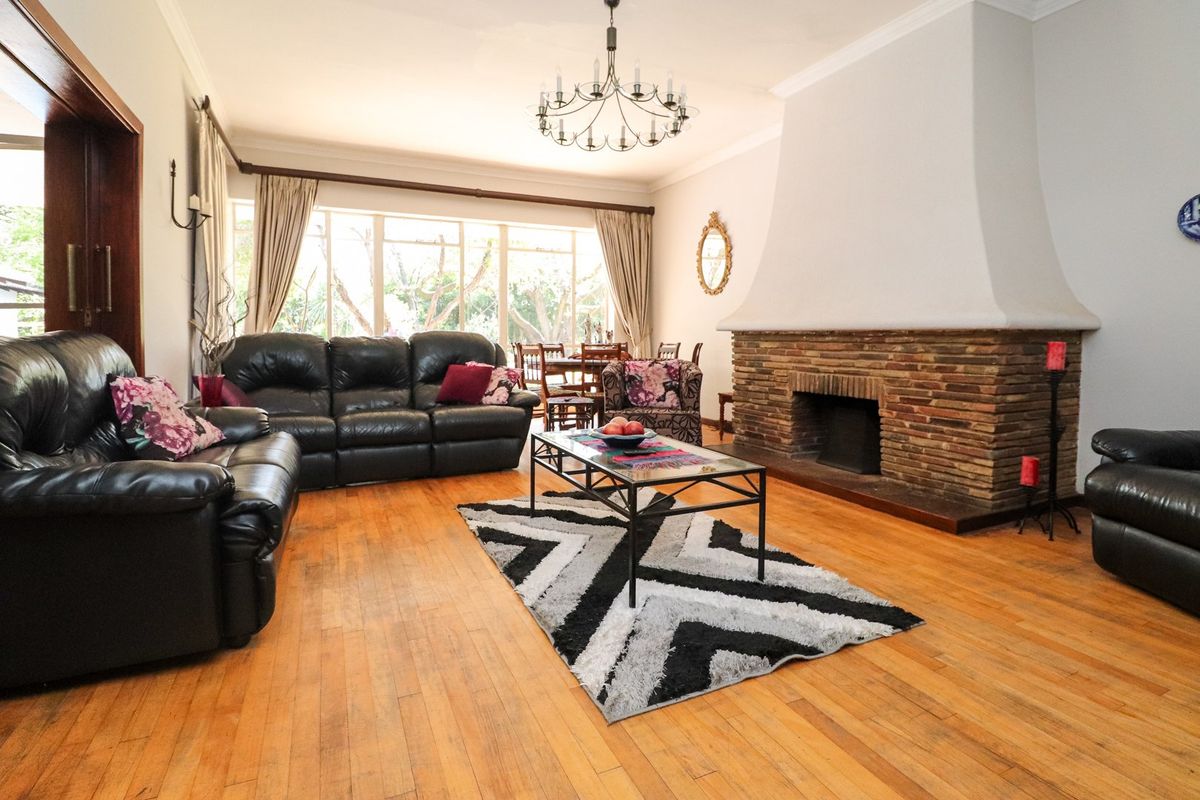 Spacious living room featuring a prominent brick fireplace, warm hardwood flooring, and large windows that provide ample natural light.