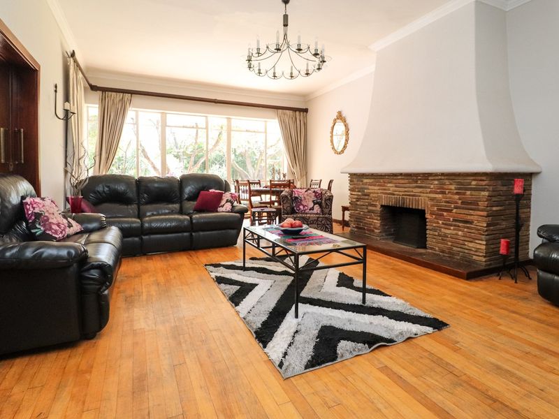 Spacious living room featuring a prominent brick fireplace, warm hardwood flooring, and large windows that provide ample natural light.