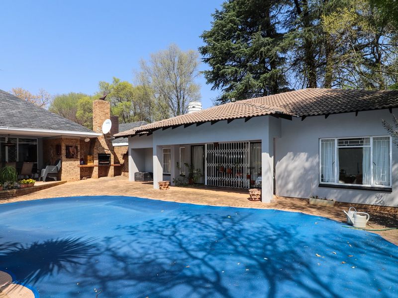 Rear exterior view featuring a swimming pool with cover, a brick built-in braai area, and a paved patio space adjacent to the house.