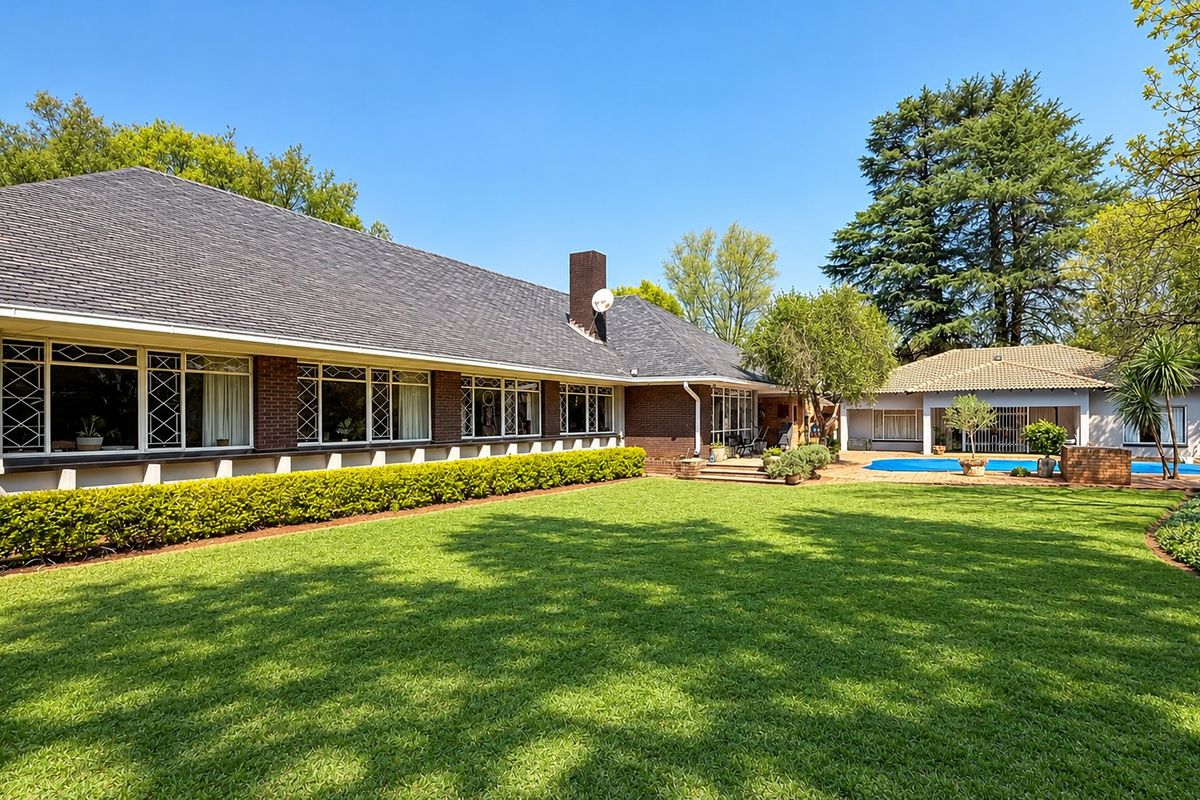 Spacious rear garden featuring a well-maintained lawn, a swimming pool, and a large brick-clad residence with a classic tiled roof.