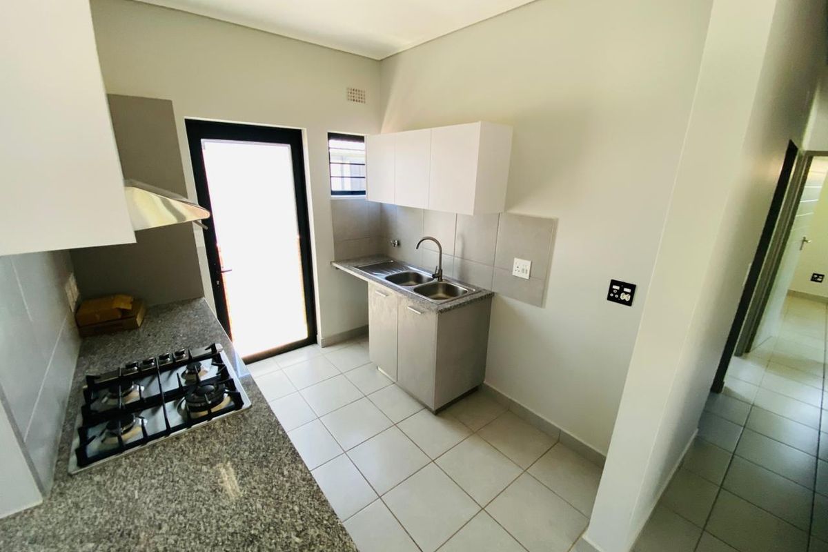 A clean, modern kitchen featuring granite countertops, a gas hob with extractor, double sink, and ample built-in cabinetry with direct outdoor access.
