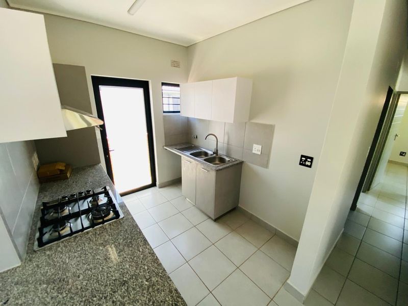 A clean, modern kitchen featuring granite countertops, a gas hob with extractor, double sink, and ample built-in cabinetry with direct outdoor access.