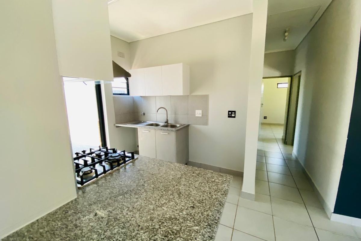 A clean, modern kitchen featuring granite countertops, a built-in gas hob, and neutral cabinetry, leading into a tiled hallway.