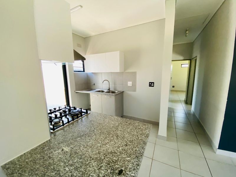 A clean, modern kitchen featuring granite countertops, a built-in gas hob, and neutral cabinetry, leading into a tiled hallway.