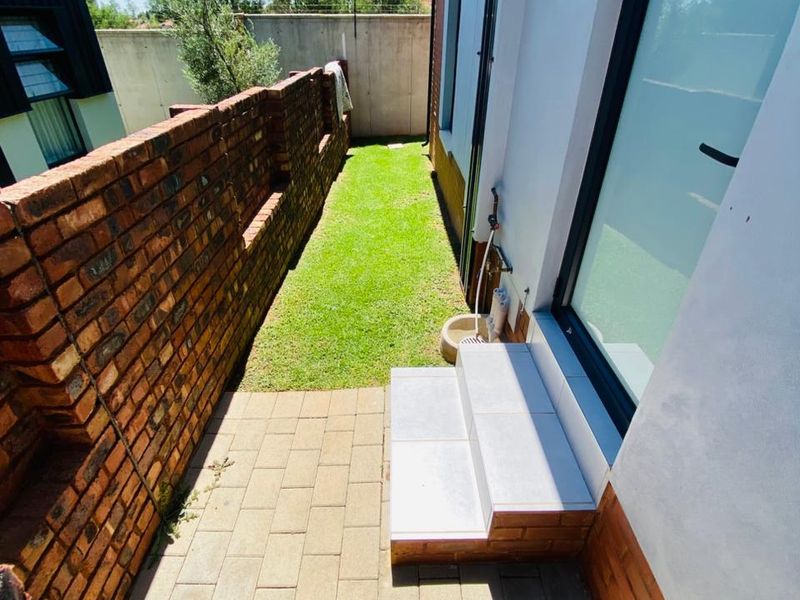 A narrow rear garden area featuring a paved walkway, a small lawn, and a brick boundary wall.