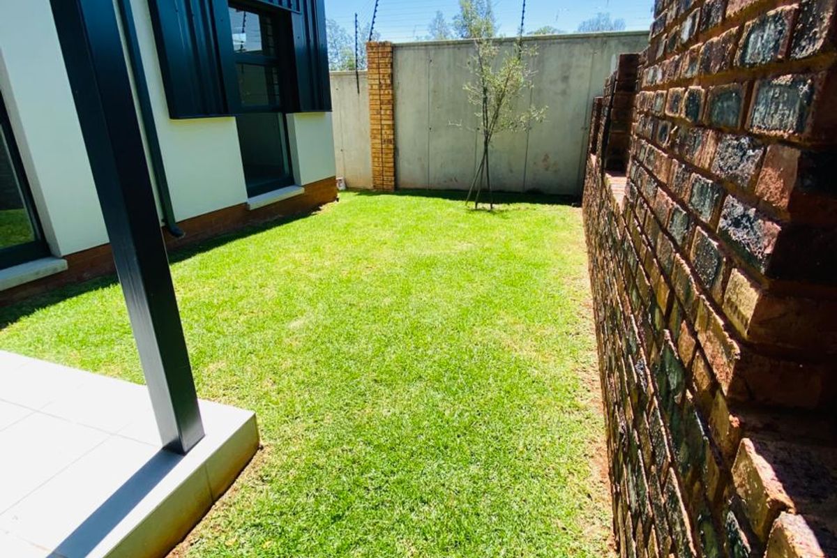 A well-maintained rear garden featuring a manicured lawn, a paved patio area, and a secure brick boundary wall with electric fencing.