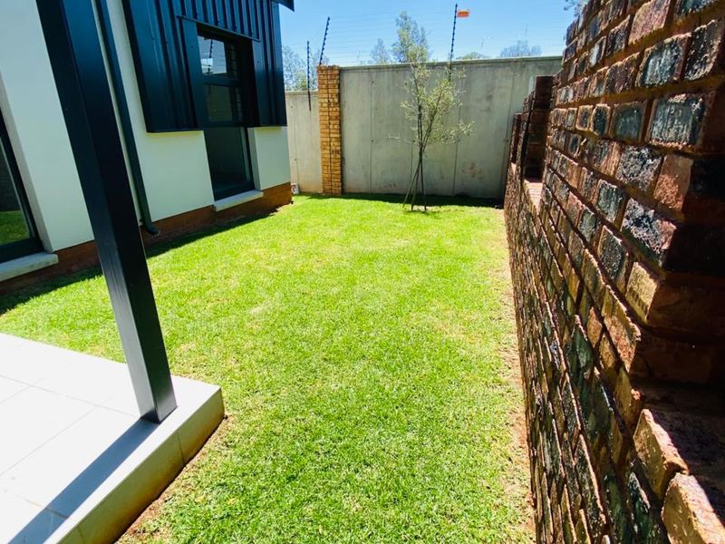 A well-maintained rear garden featuring a manicured lawn, a paved patio area, and a secure brick boundary wall with electric fencing.