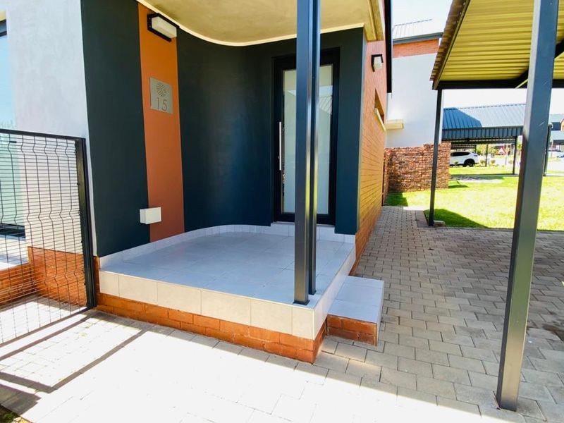 Modern front entrance featuring a covered porch with tiled flooring, steel support column, and adjacent paved driveway with a carport.