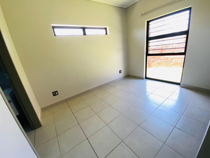 A bright, empty bedroom featuring neutral tiled flooring, a horizontal clerestory window, and a large window with security bars.