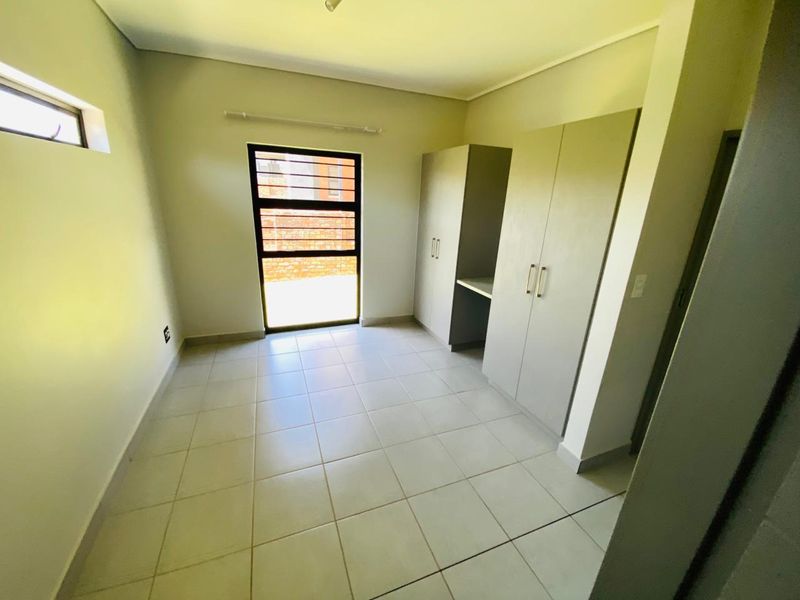 A clean, empty bedroom featuring neutral tiled flooring and built-in cupboards, offering a bright and versatile space ready for personalization.