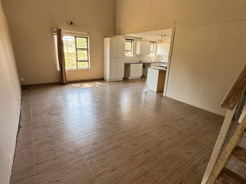 Spacious open-plan living area featuring wood-look tiled flooring, a staircase, and an adjoining kitchen with built-in cabinetry.