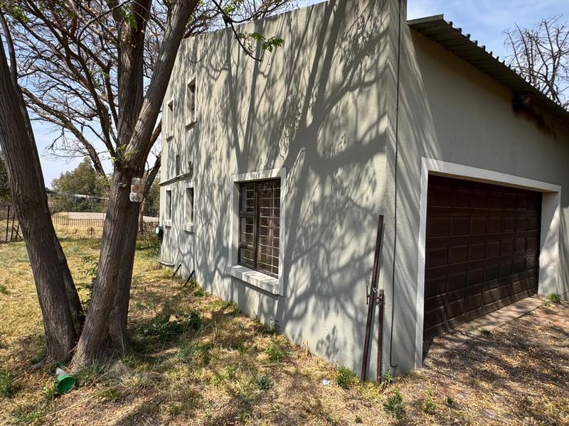 Exterior view of a detached garage building featuring a sectional door and steel-framed windows with security bars, set in a natural garden environment.