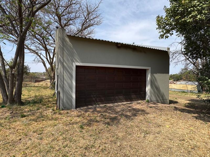 A detached single-car garage featuring a sectional door and corrugated metal roofing, situated in a natural, unlandscaped outdoor setting.