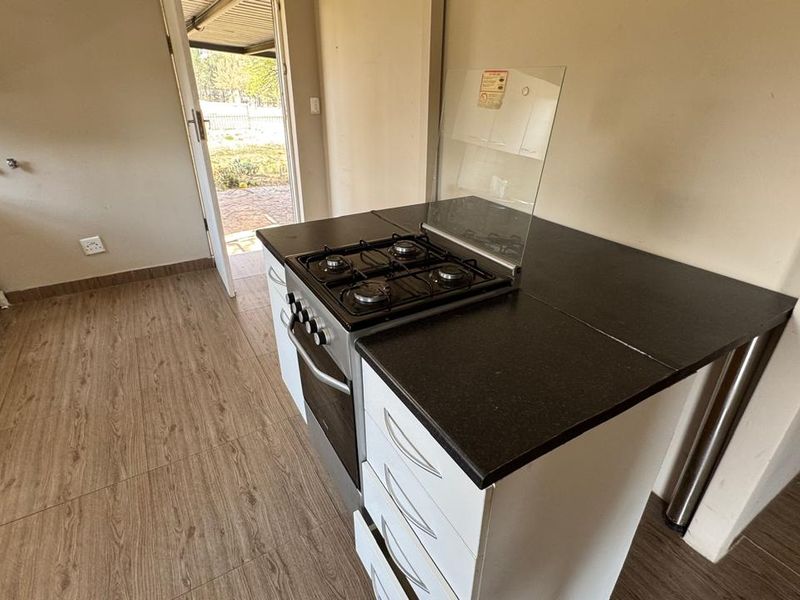 A functional kitchen area featuring a built-in oven, gas hob, and modern laminate flooring, with direct access to an outdoor space.