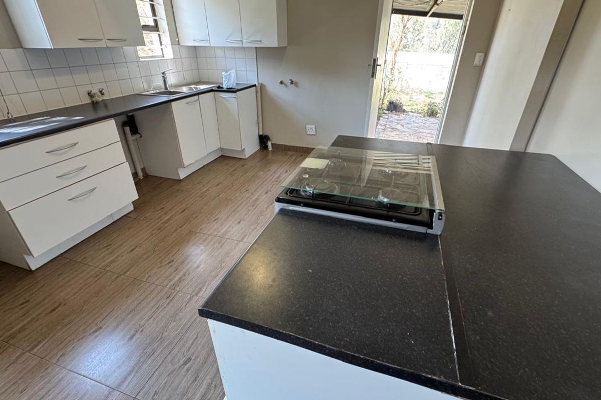 A functional kitchen featuring white cabinetry, dark laminate countertops, a gas hob, and tiled flooring with direct access to the exterior.