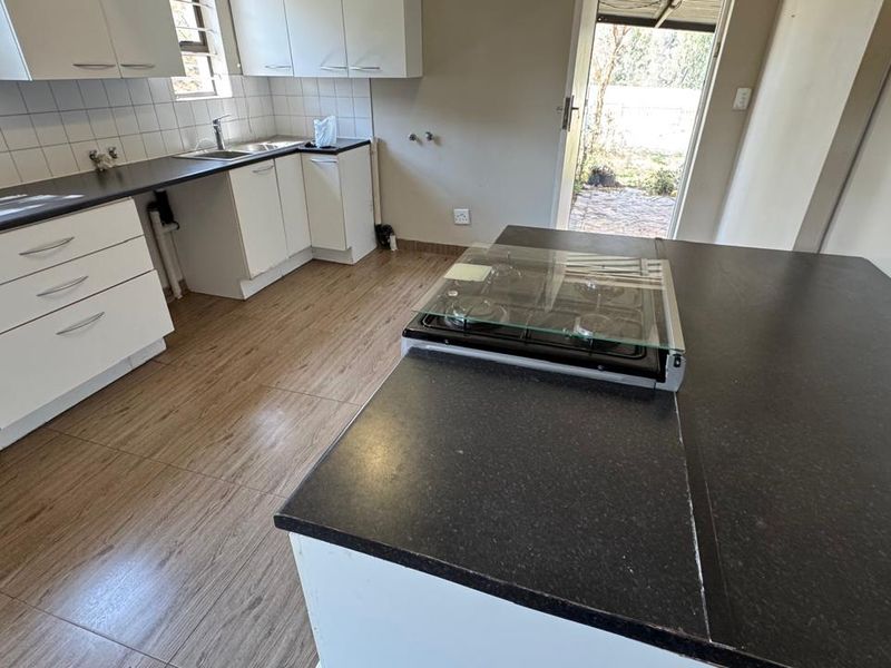 A functional kitchen featuring white cabinetry, dark laminate countertops, a gas hob, and tiled flooring with direct access to the exterior.