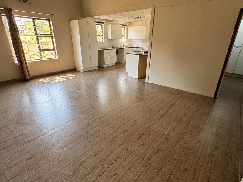 Spacious open-plan living area featuring wood-look floor tiles and an integrated kitchen with built-in cabinetry and island, offering a versatile layout.