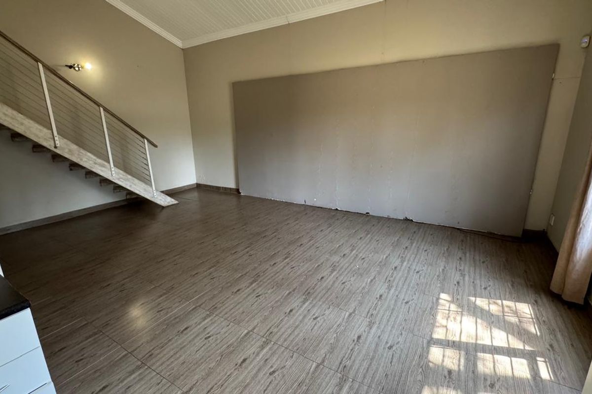 An empty living room featuring wood-look laminate flooring, a staircase with a metal railing, and a large wall panel, offering a blank canvas for renovation.