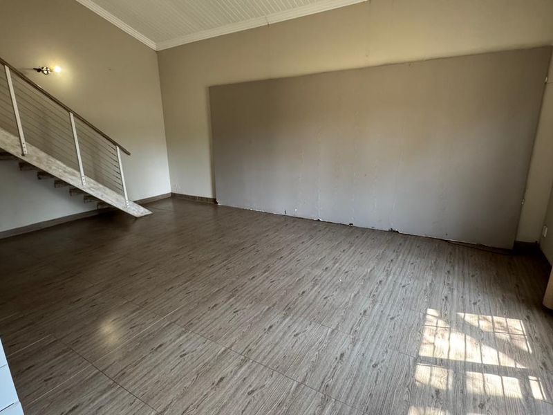 An empty living room featuring wood-look laminate flooring, a staircase with a metal railing, and a large wall panel, offering a blank canvas for renovation.