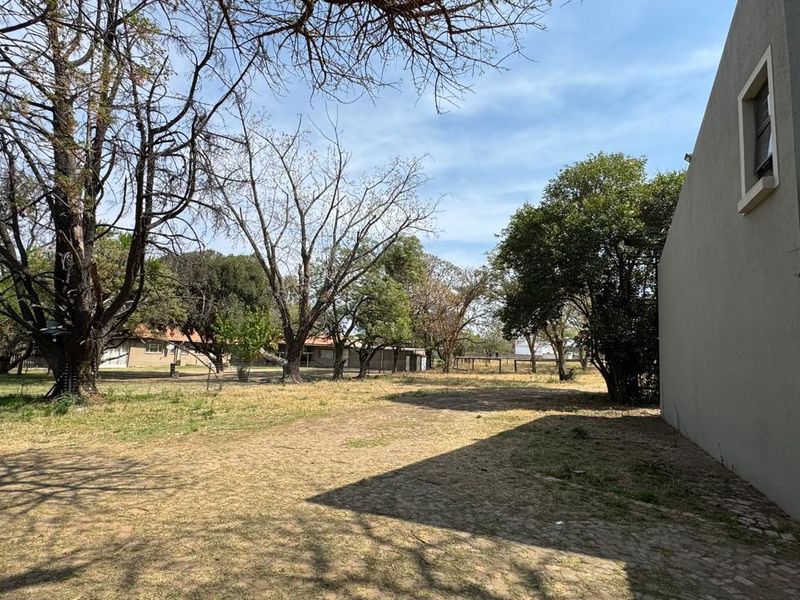 A view of the rear exterior area featuring a paved section, a wall-mounted air conditioning unit, and a spacious garden with mature trees.