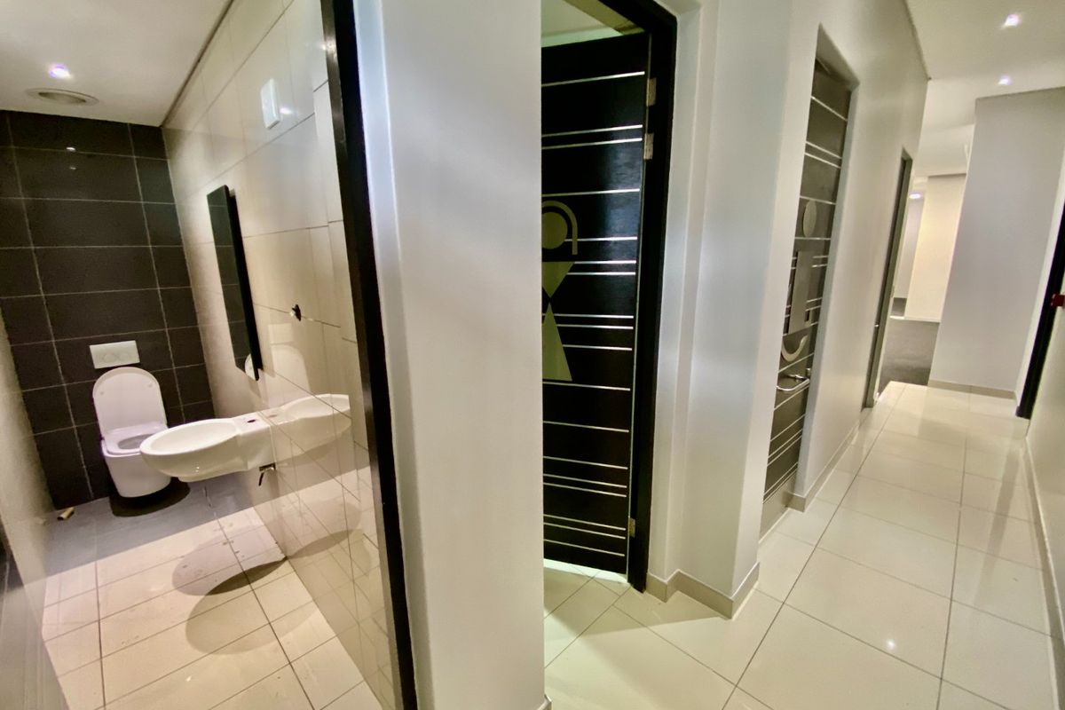 Modern commercial bathroom facility featuring wall-mounted sanitary ware, sleek tiled finishes, and recessed lighting in a clean, well-maintained corridor setting.