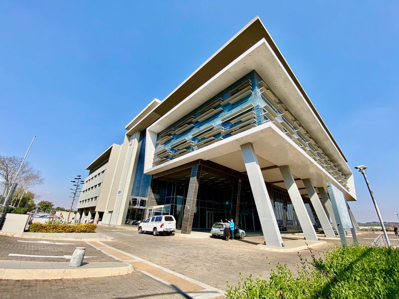 Modern commercial office building featuring a striking cantilevered design, glass facade with sun louvers, and a paved entrance area.