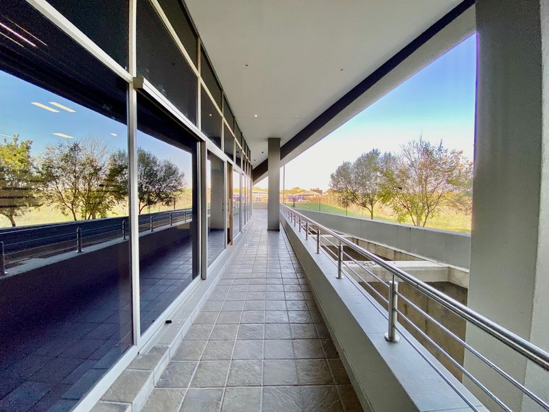 A modern, covered commercial balcony featuring tiled flooring, a stainless steel balustrade, and an expansive glass facade overlooking the surrounding landscape.
