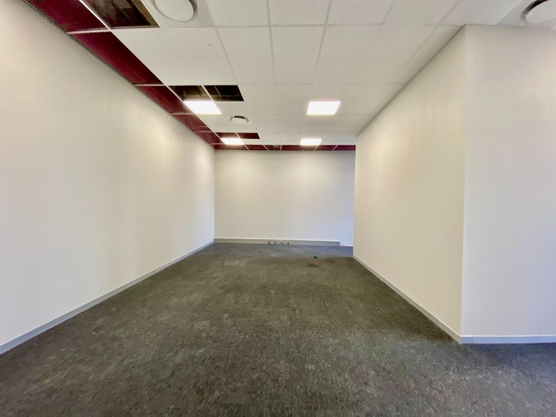 An empty commercial office space featuring carpeted flooring, recessed lighting, and a suspended ceiling with some missing tiles requiring repair.