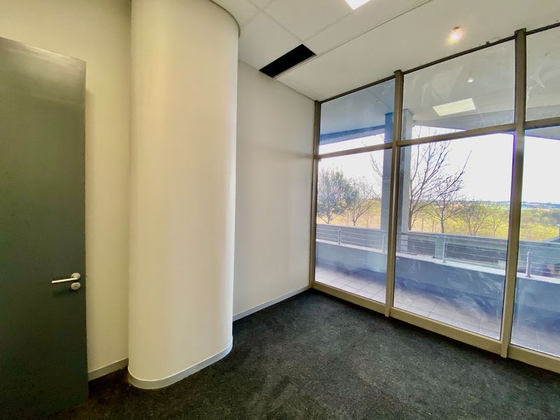 A bright, empty office space featuring floor-to-ceiling windows, a curved structural column, and neutral finishes, suitable for a professional workspace.